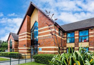 Exterior view of Kingfisher care home displaying a clean and peaceful environment, a tall brick building with a garden surrounding the entrance