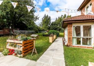 A rear garden featuring vibrant decoration and plants with tables and benches for the residents to relax on at Roseway House care home