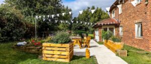 A rear garden featuring vibrant decoration and plants with tables and benches for the residents to relax on at Roseway House care home